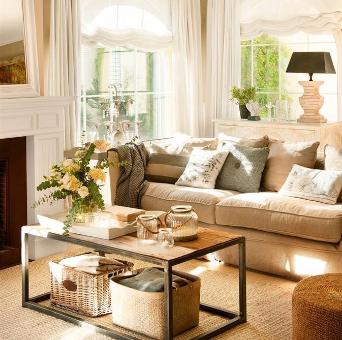 Salón en tonos neutros con sofá beige, cojines grises y marrones, mesa de centro y flores