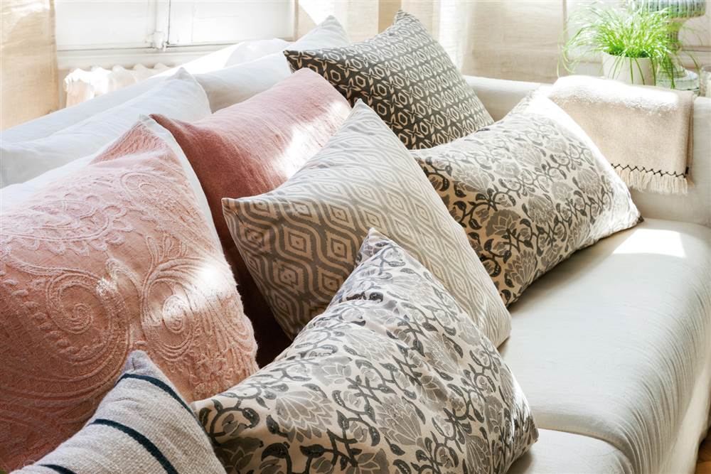 Cojines en rosa, gris y verde con estampados florales y bordados sobre sofá blanco