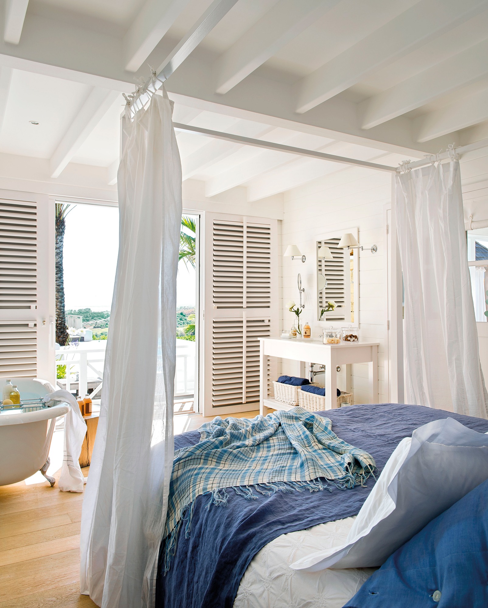 Dormitorio en blanco y detalles en azul con bañera con vistas al jardín_365839