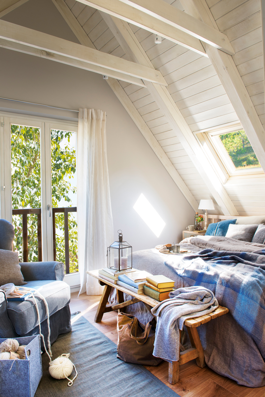 00442701. Dormitorio abuhardillado rústico con techos de madera en blanco, butaca gris y ropa de cama azul y gris 00442701