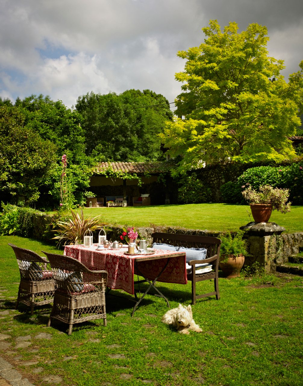 Comedor exterior en medio del prado con banco y sillones de mimbre