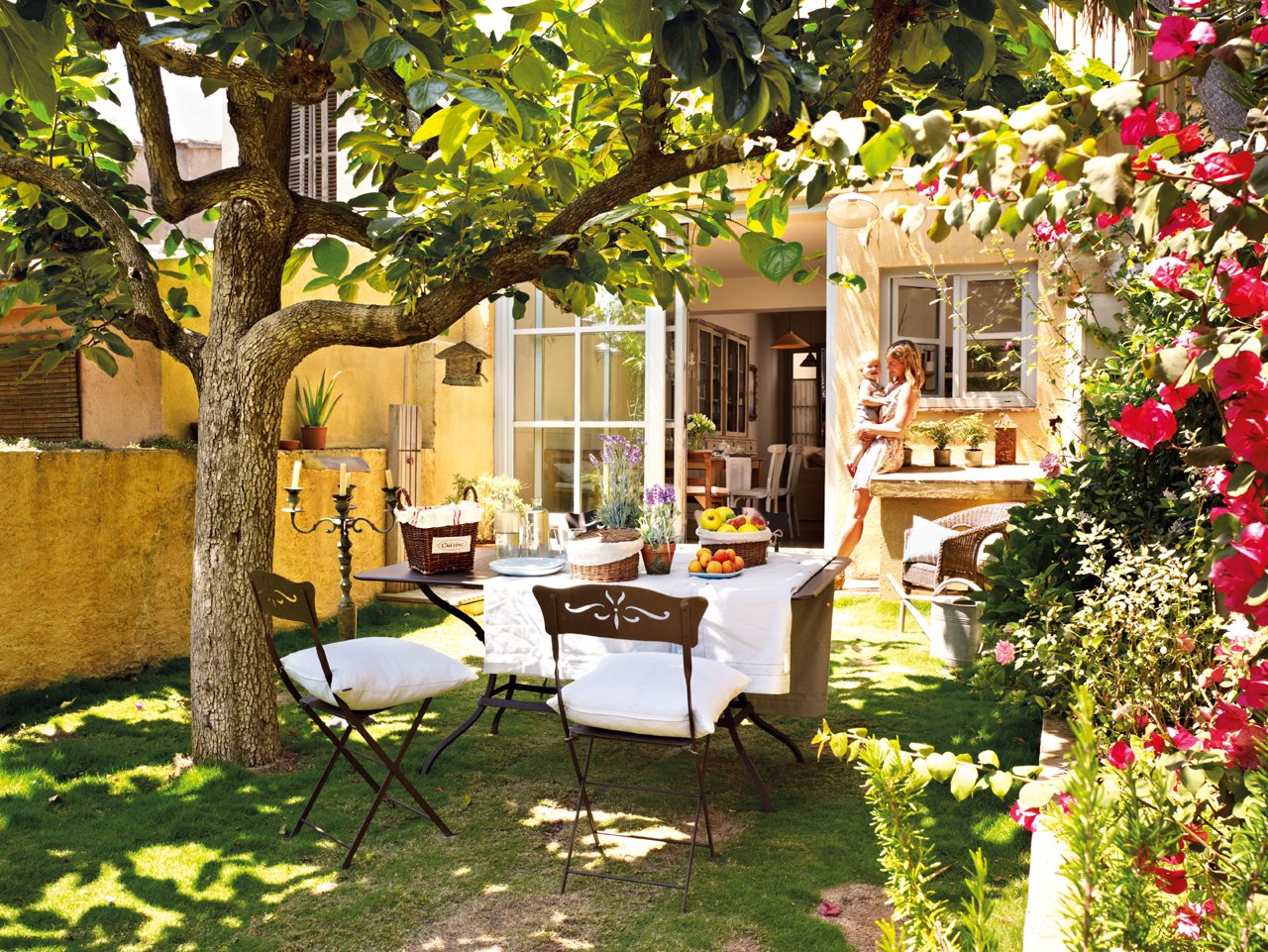 Comedor exterior en el patio con sillas de hierro y textiles en tonos blancos. 