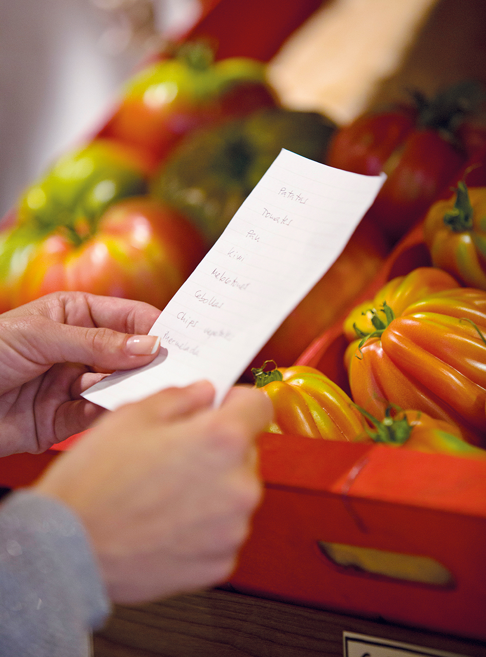 Detalle de manos sujetando lista de la compra y tomates de fondo