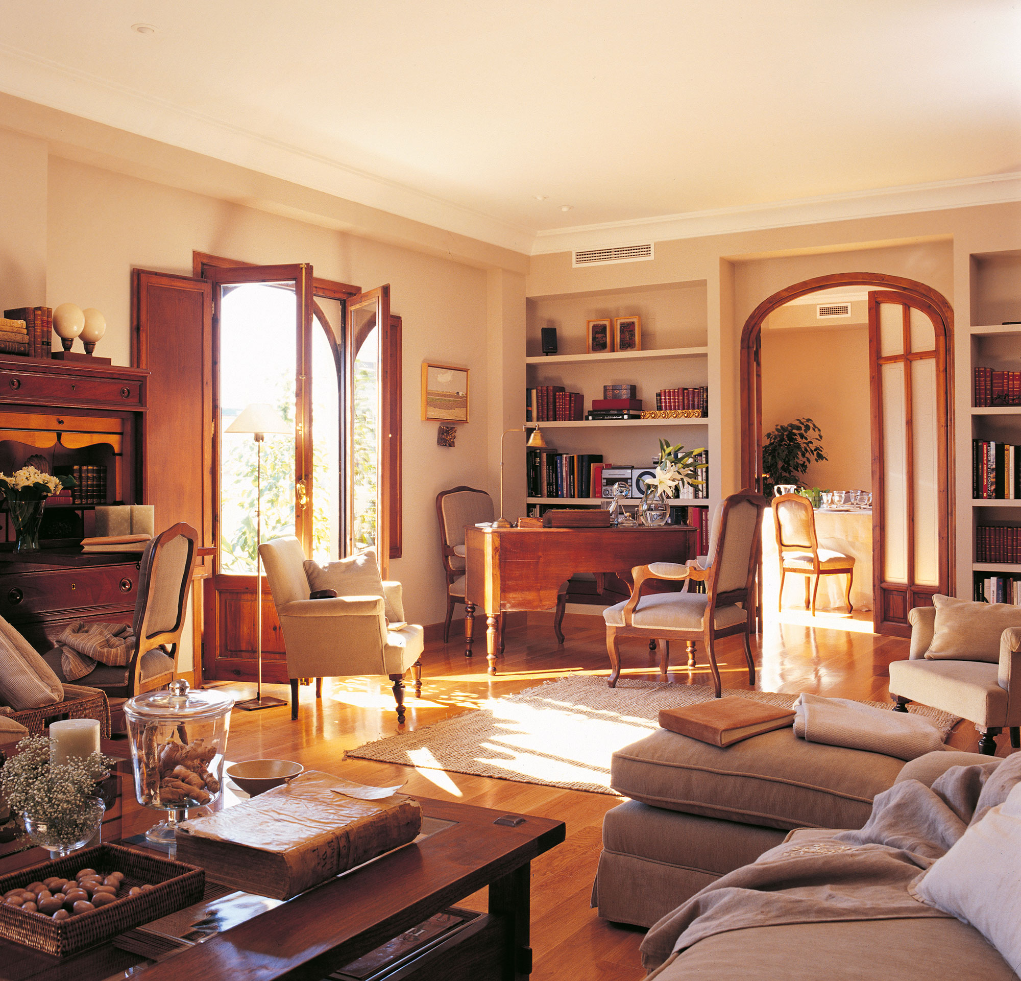 Salón clásico con sofá beige con chaise longue y muebles de madera oscura. 