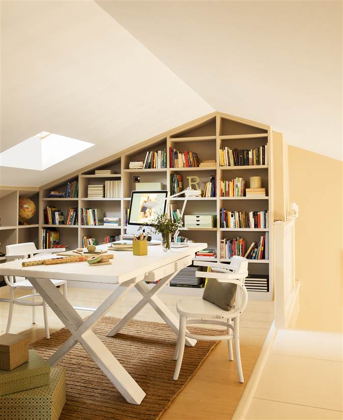 Buhardilla en blanco habilitada como zona de estudio con mesa de trabajo, ordenador y librería