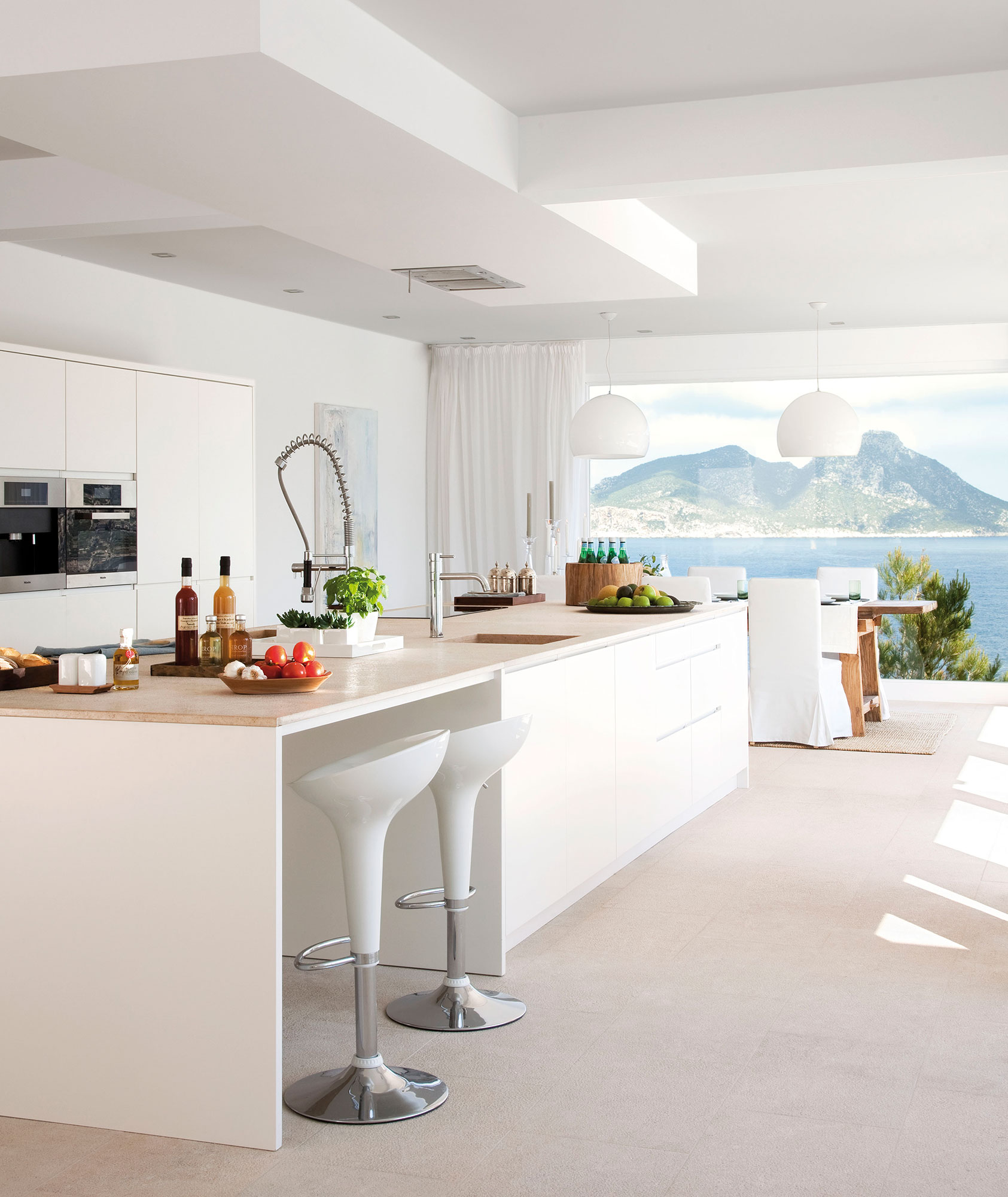 Cocina blanca con isla y con vistas al mar.