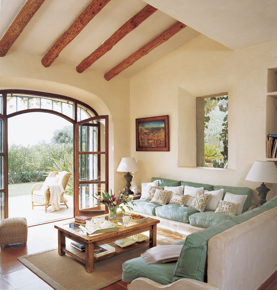 Salón con sofás de obra y cojines verdes y gran ventanal al porche
