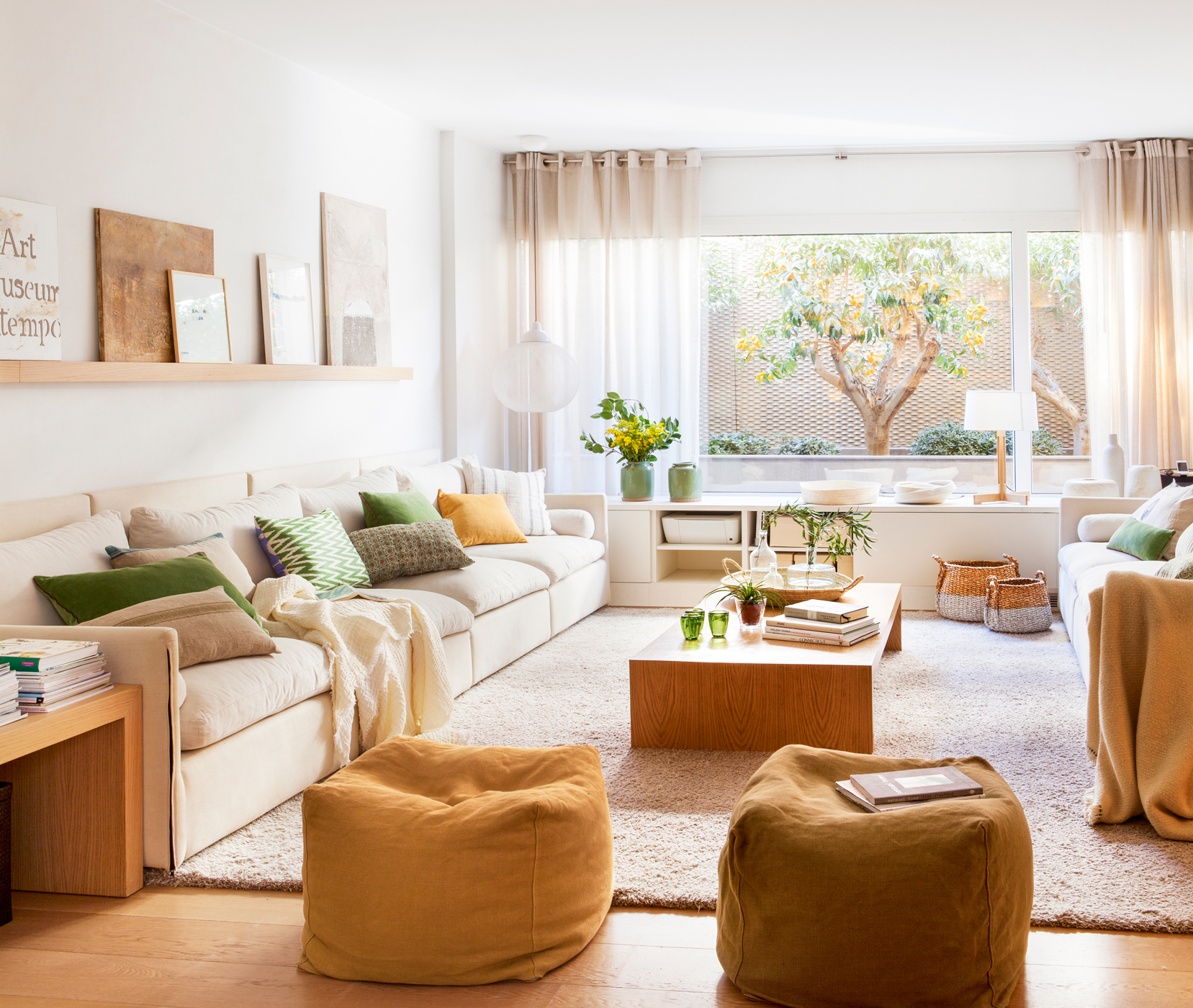 Salón con sofá blanco largo, puffs amarillos, mueble bajo la ventana y mesa de centro de madera.