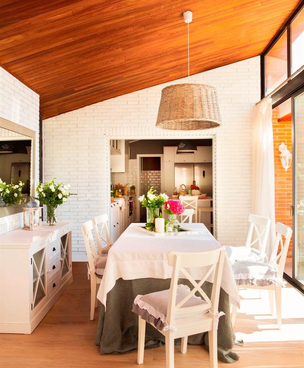 Comedor con acceso a la cocina con pared de ladrillo blanco, cómoda, espejo, techo de madera, lámpara de fibra