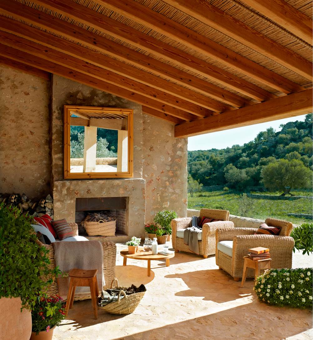 Porche con chimenea, pared de piedra, sillones y sofás de fibra natural y espejo bajo techo de madera