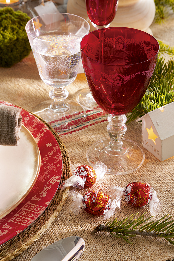 Detalle de mesa de Navidad con copas rojas y vajilla blanca y roja