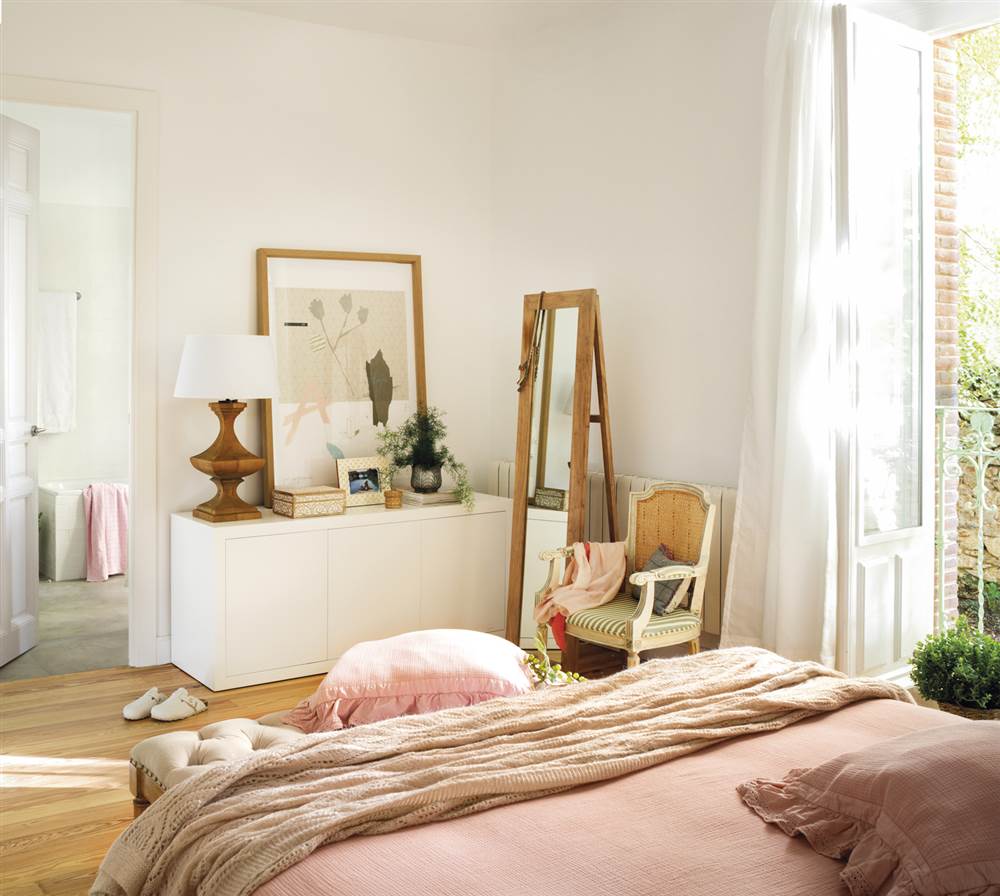 Dormitorio con cómoda blanca y cama con plaid beige y sábanas rosas