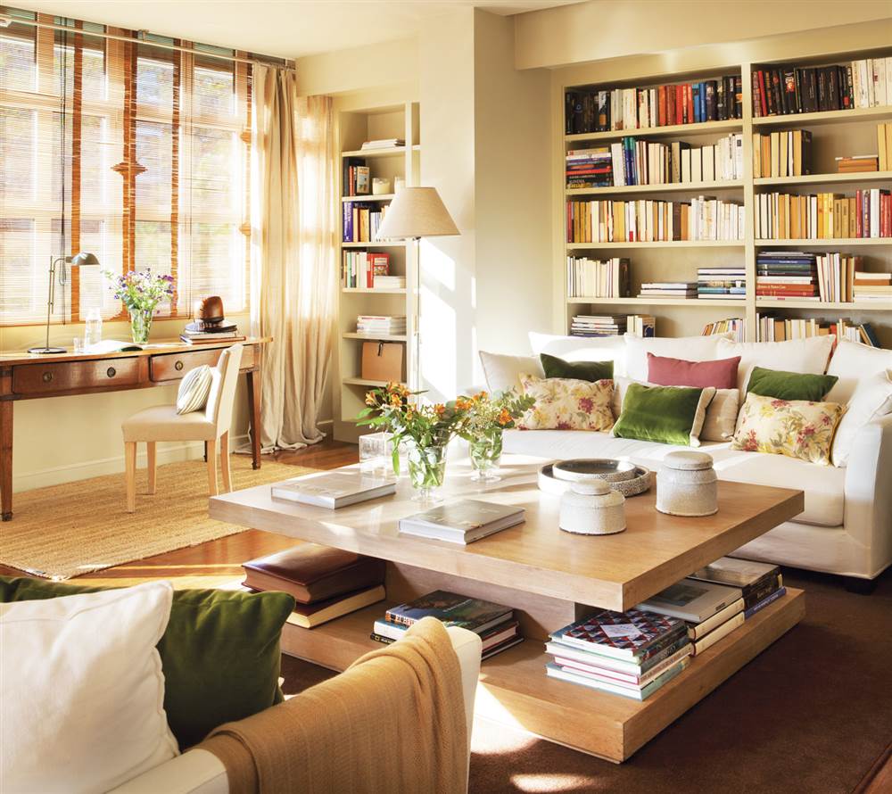 Salón con sofá blanco, cojines en verde, mesa de centro de madera y librería de obra