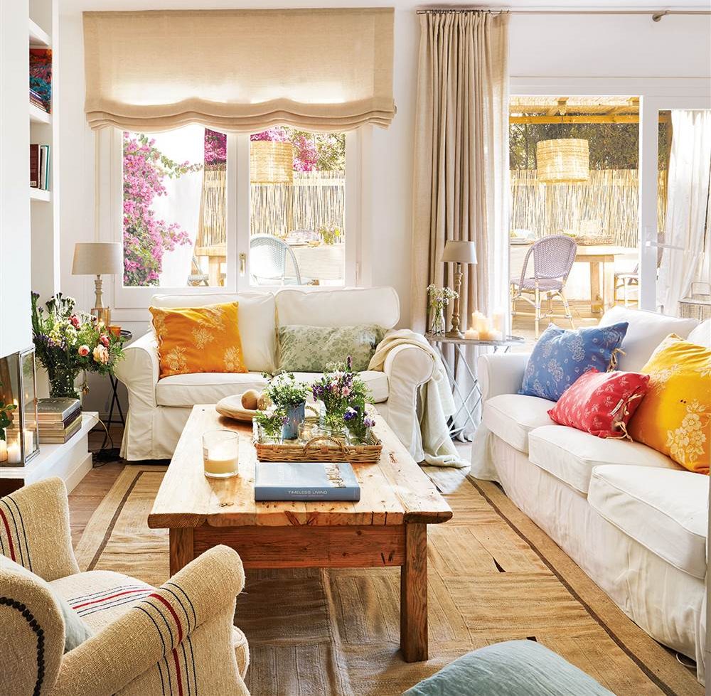 Salon con cojines de colores vivos sobre sofa blanco y mesa de centro de madera envejecida