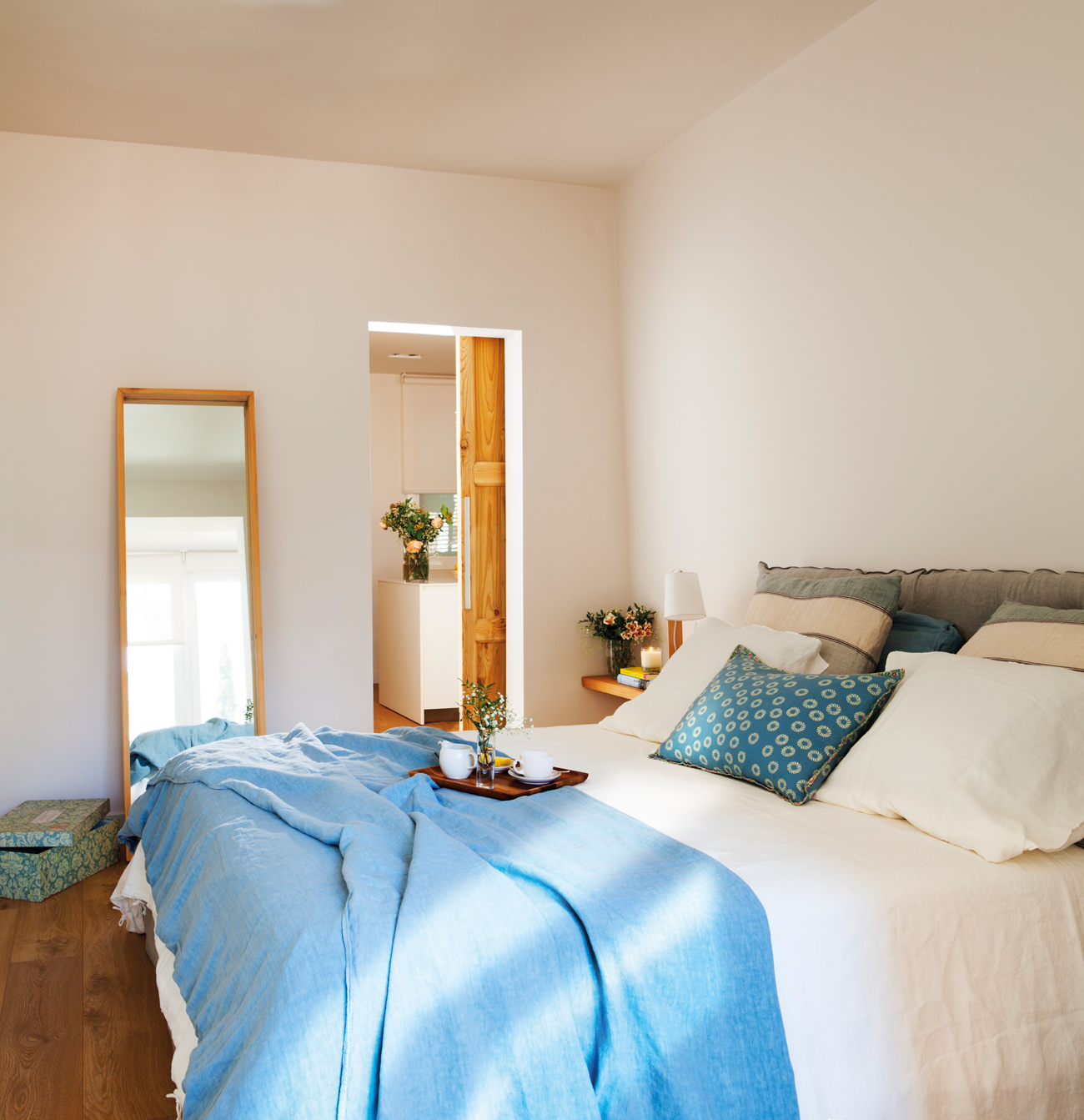 Dormitorio con cabecero y ropa de cama azul y espejo en la pared.