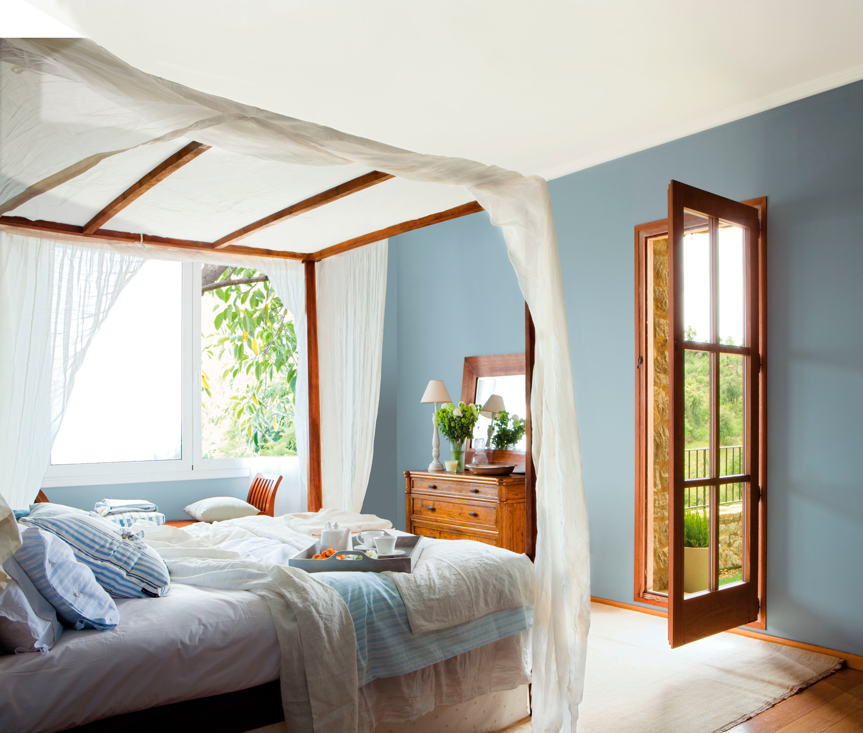 Dormitorio de verano con dosel de madera y pared en azul.