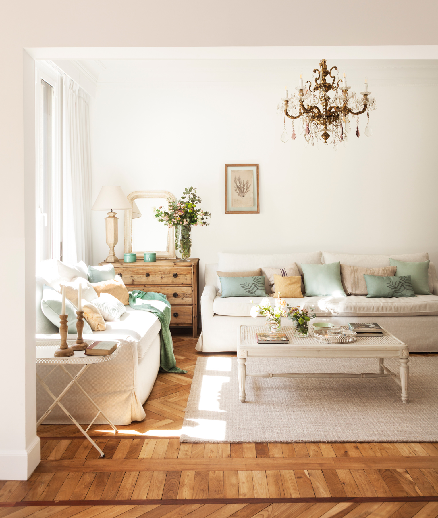 Salón clásico con suelos de madera, sofás blancos y lámpara de araña. 