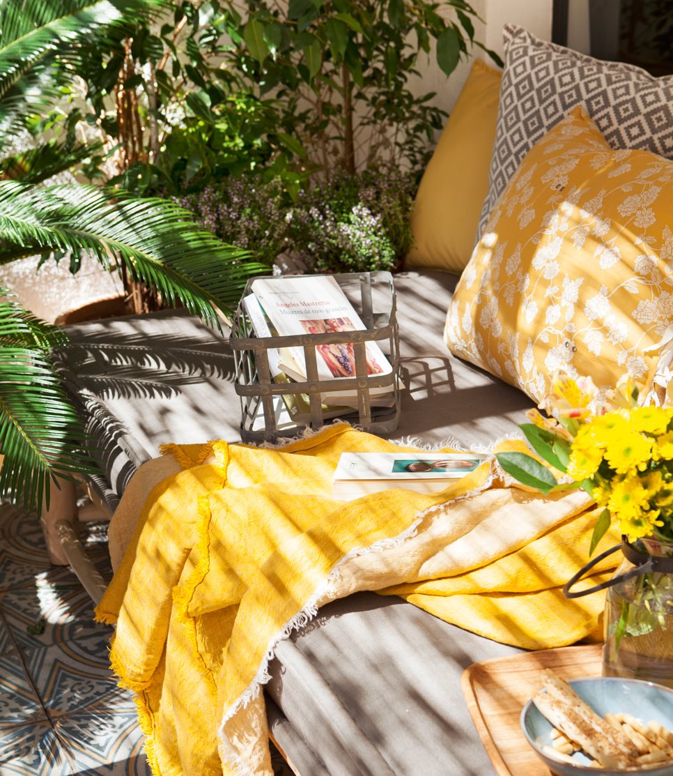 Detalle de sofá exterior con cojines y plaid amarillo, cojín gris y blanco, suelo hidráulico, bandeja y plantas_433263
