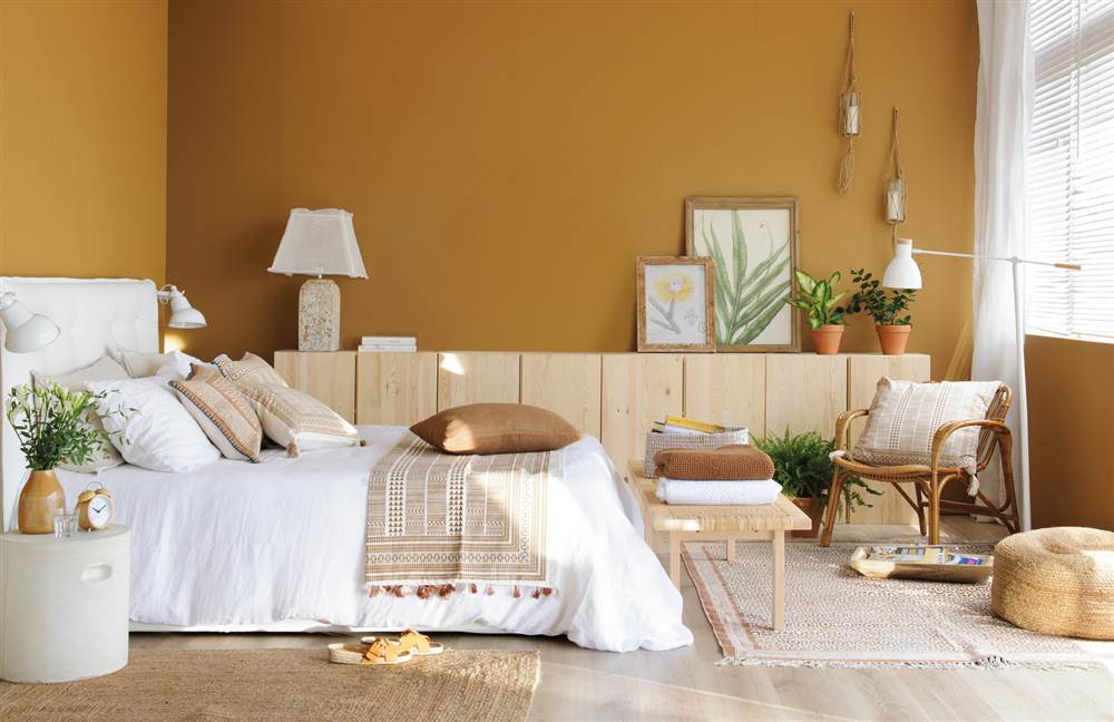 Dormitorio en color caramelo y blanco, con aparador y banqueta de madera, butaca de bambú, puf de fibra y alfombras