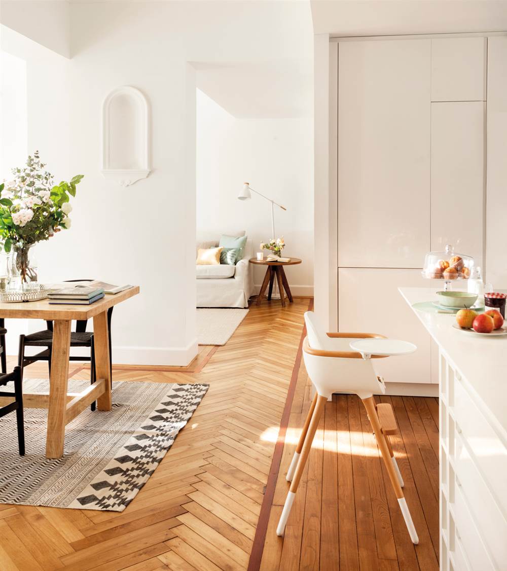 Salón, cocina y comedor con parquet en diseño de espiga y de tablillas, con paredes en blanco, taburetes de diseño y alfombra en blanco y negro