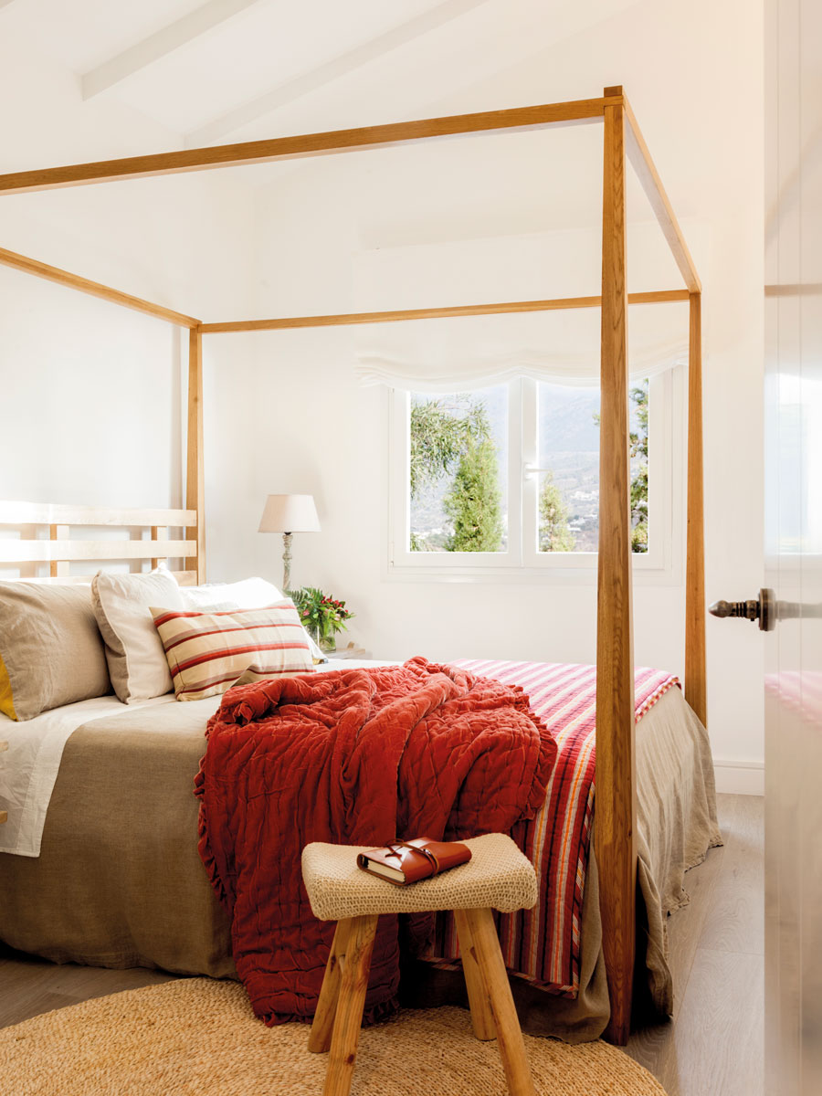 Dormitorio con cama con dosel de madera y taburete de madera con asiento tejido. 