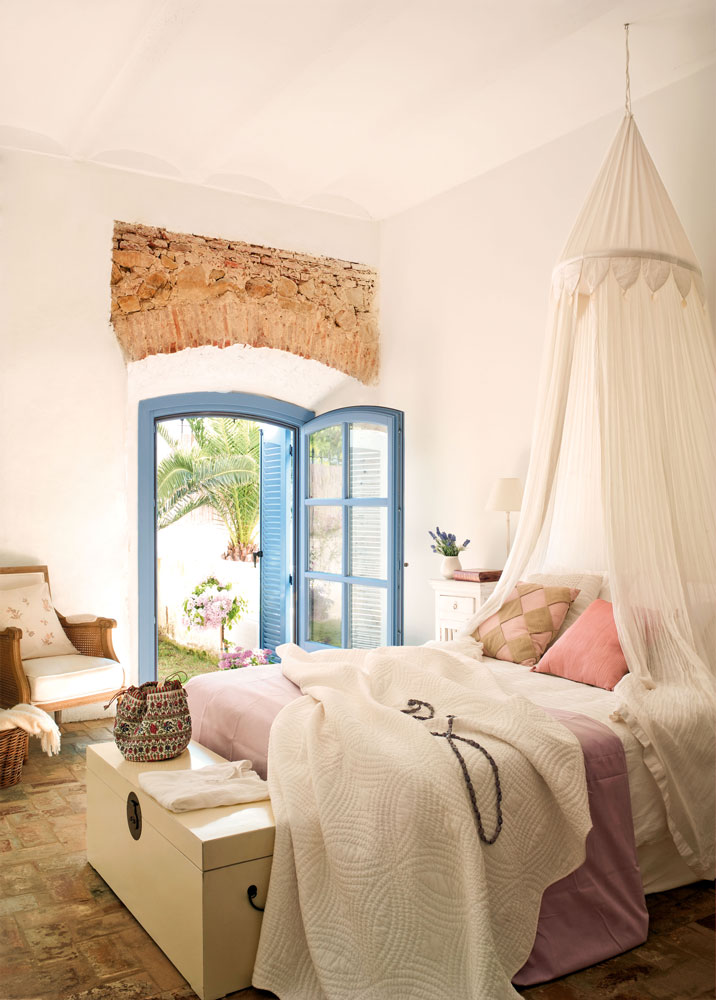 Dormitorio de estilo romántico y mediterráneo con cama con dosel de tela blanca