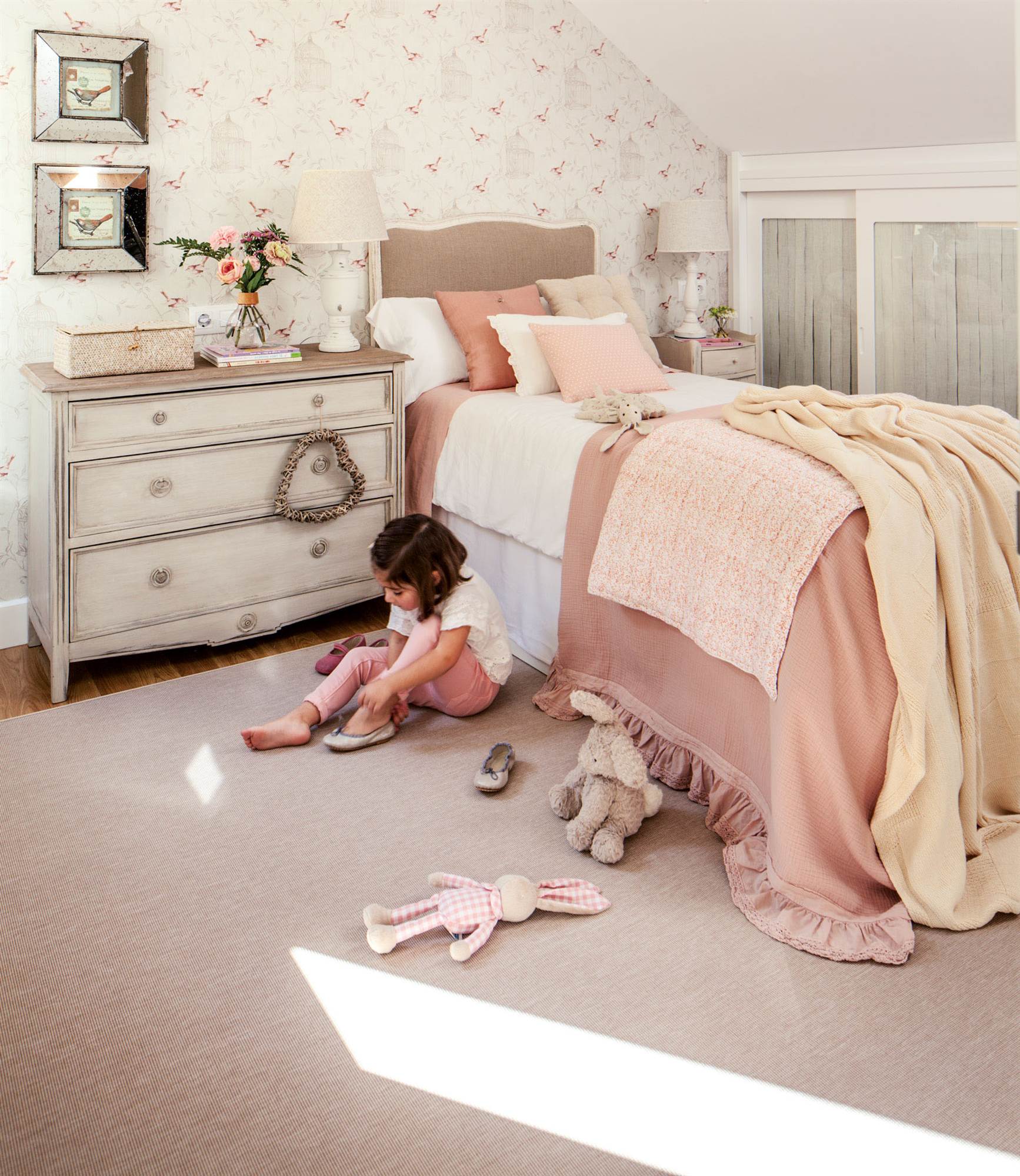 Habitación infantil de estilo romántico en tonos rosas con papel pintado, cómoda provenzal y cabecero de cama de tela