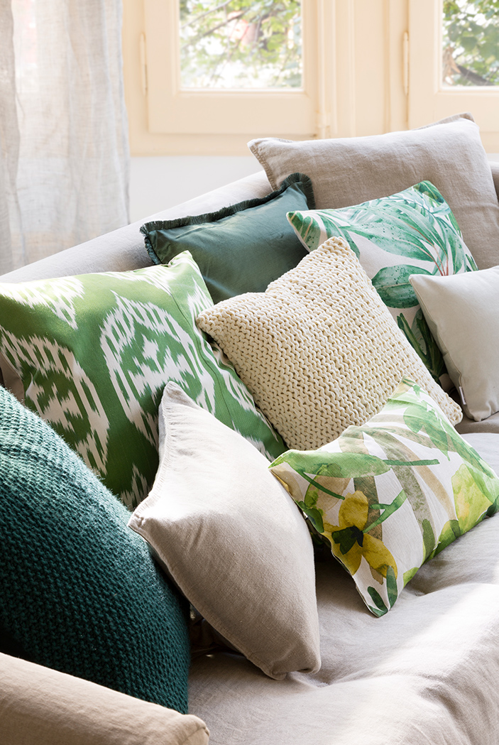Sofá beige con cojines verdes de distintos estampados y texturas. 