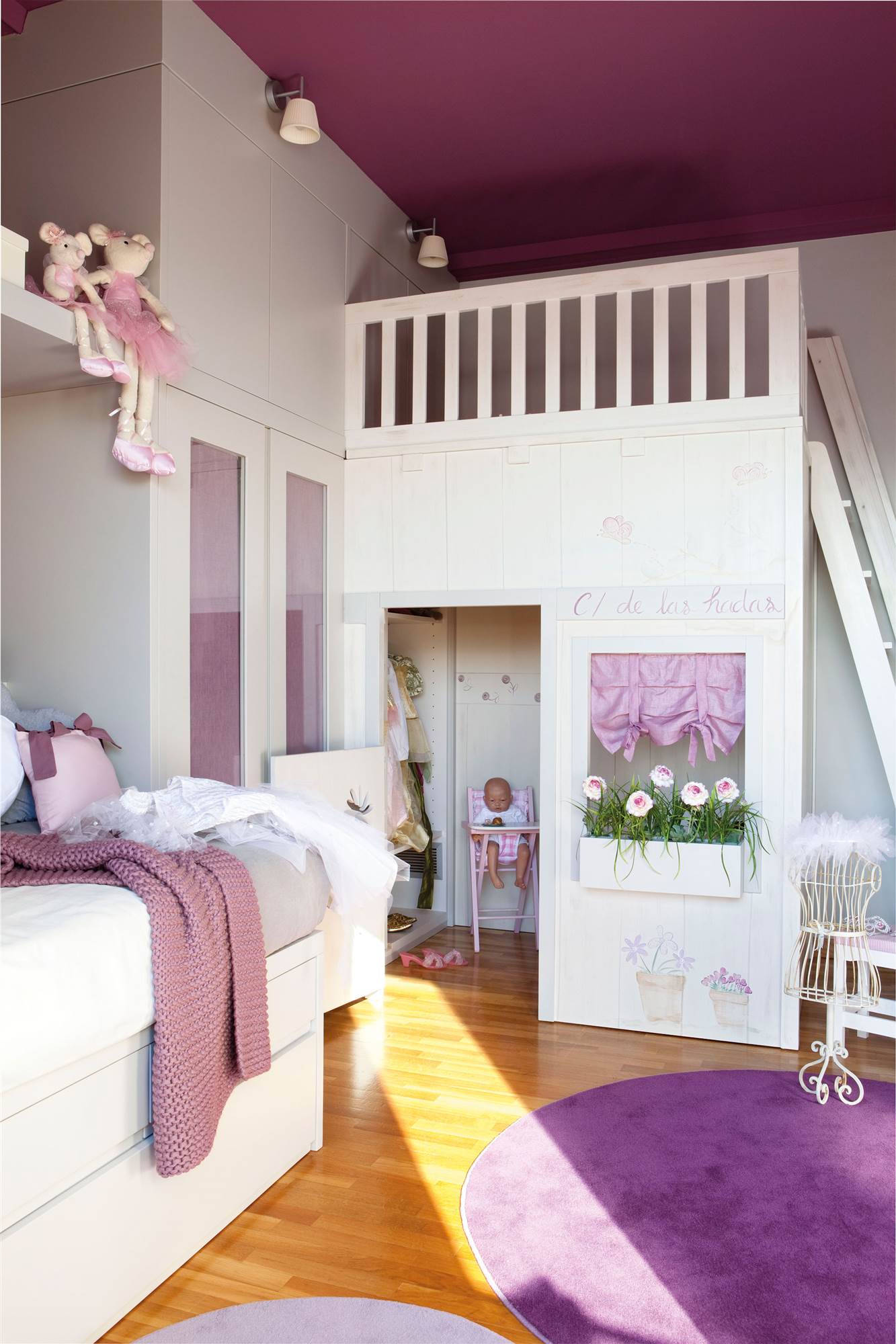 Dormitorio infantil en morado con silla con cajones, alfombras y altillo con espacio para guardar.