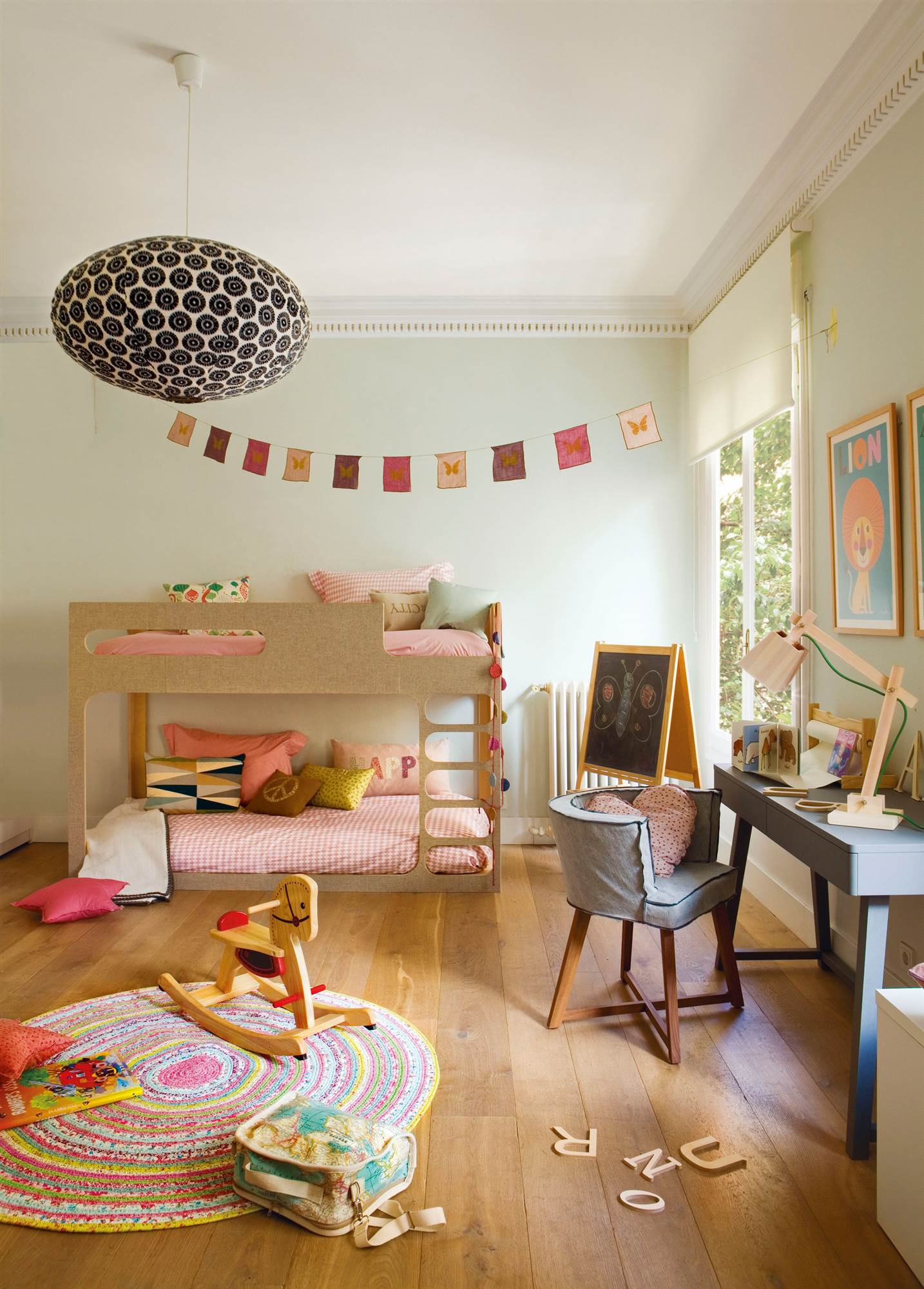 Habitación infantil colorida con litera, escritorio con silla, alfombra multicolor y guirnalda.