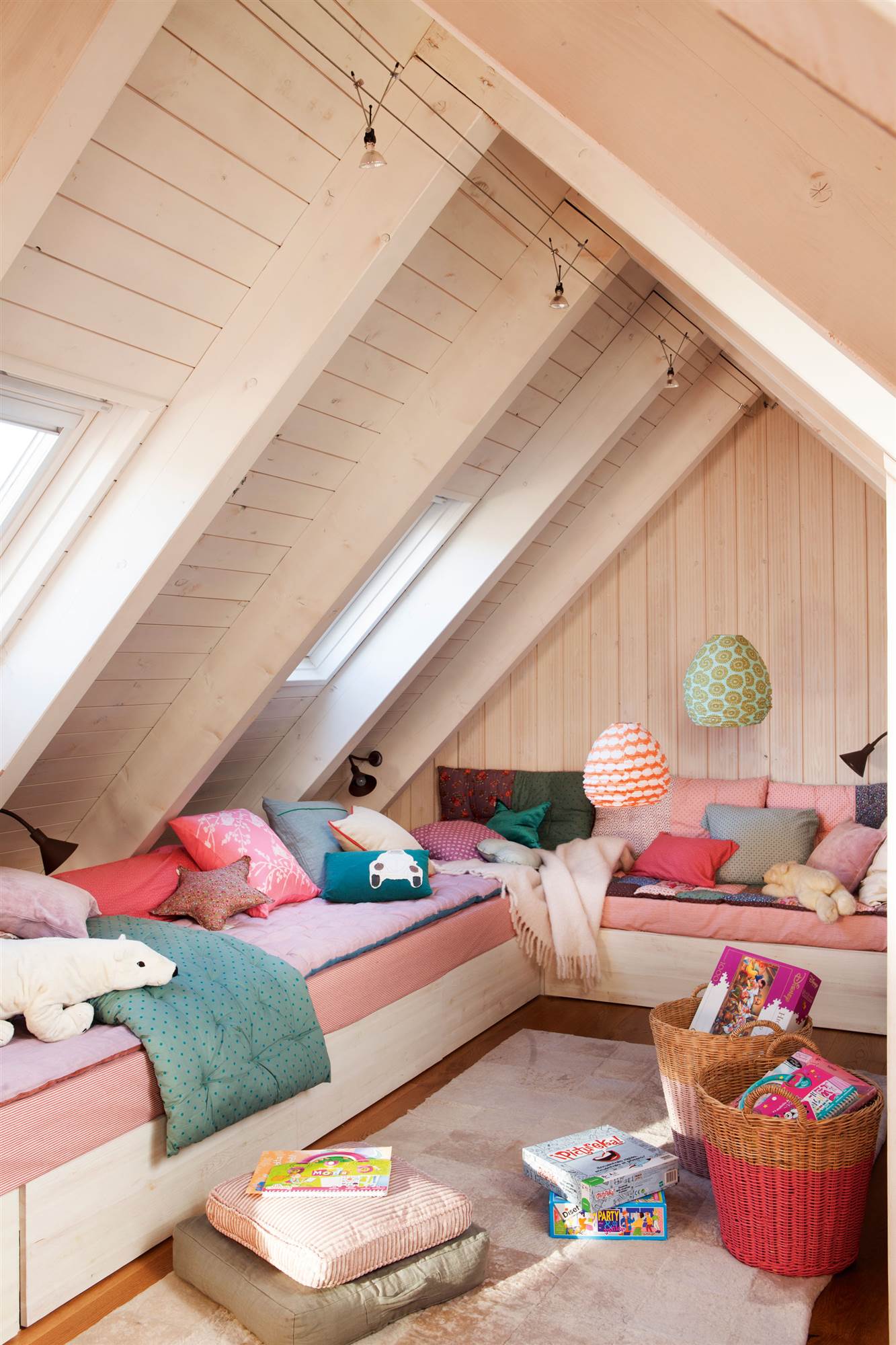 Dormitorio infantil en buhardilla con dos sofás camas en forma de L con colchoneta rosa.