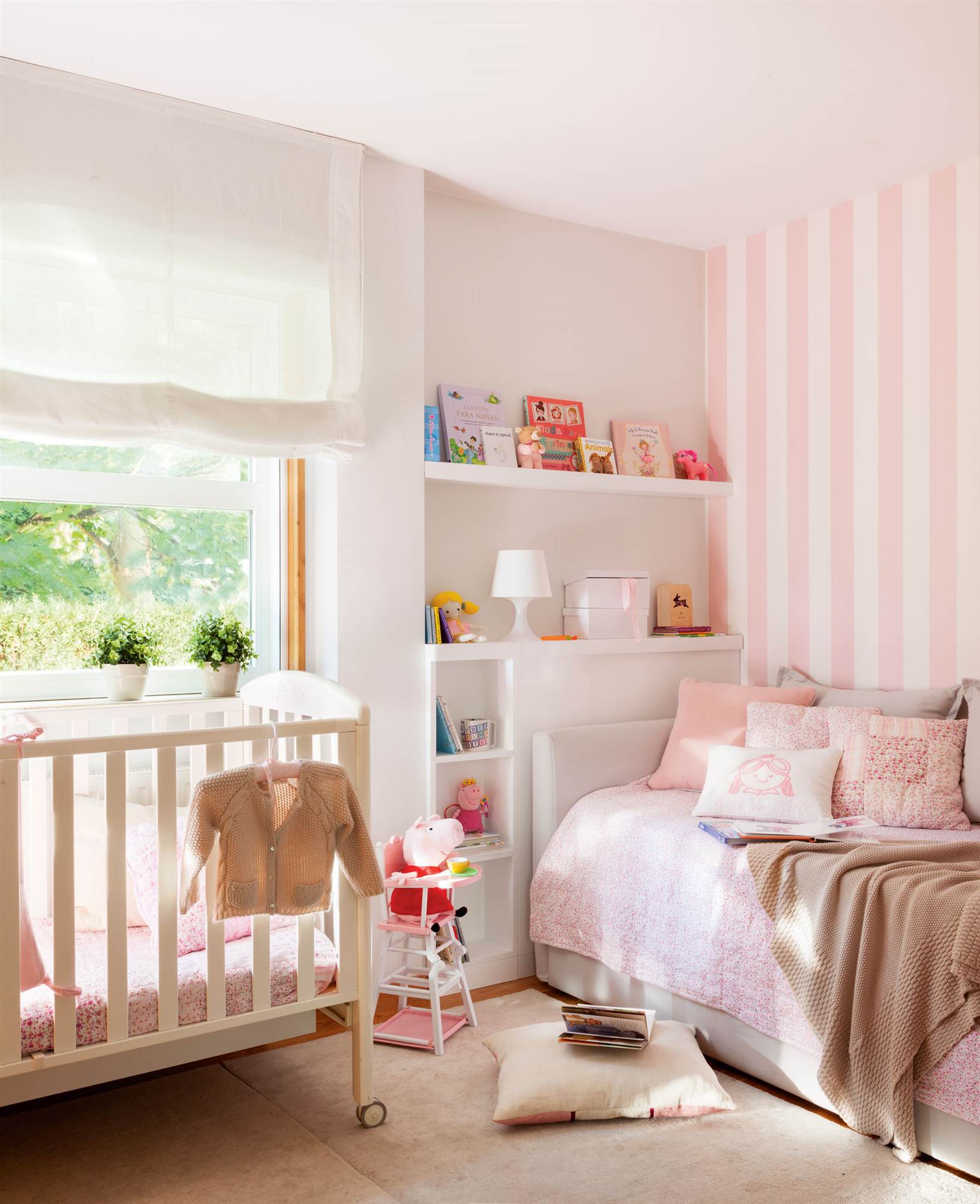 Dormitorio infantil con papel pintado rosa a rayas, ropa de cama a jeugo y cunita.