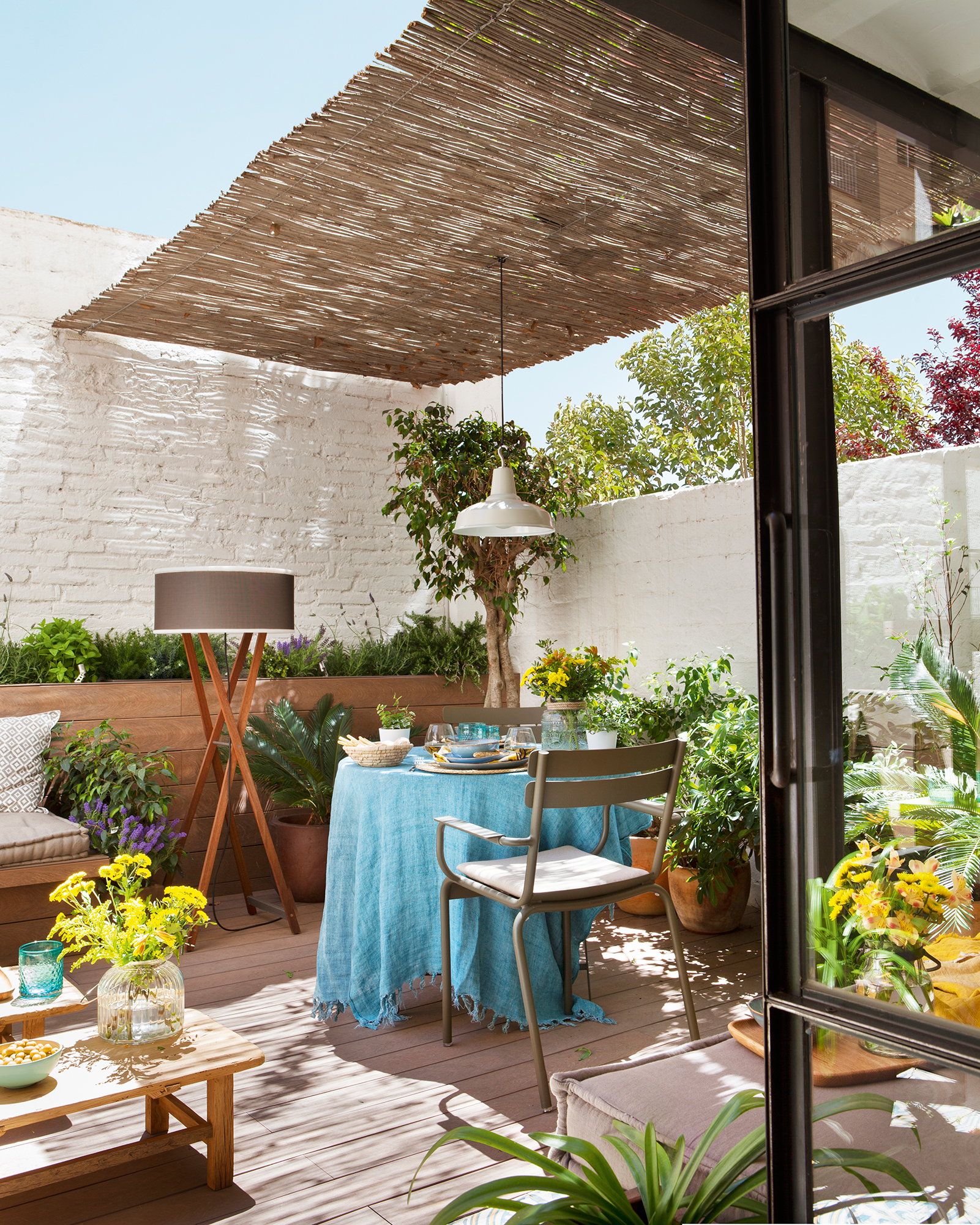 Terraza con paredes blancas y comedor de verano bajo pérgola con techo de cañizo