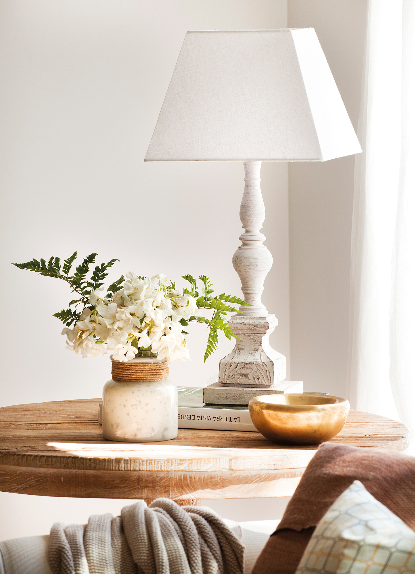 Mesa auxiliar con lámpara blanca y jarrón con flores.