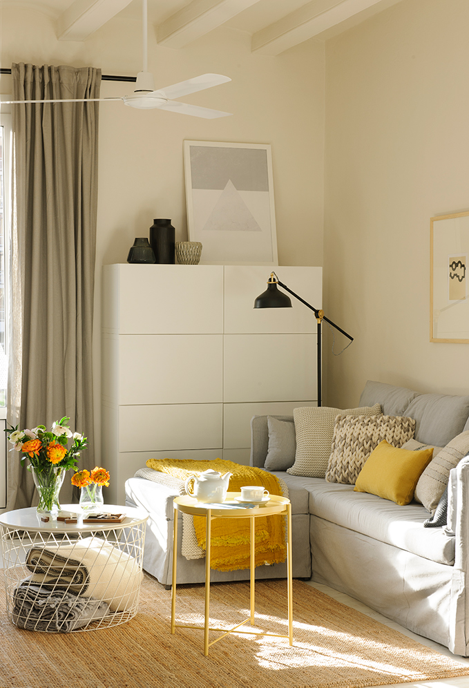 Salón pequeño con sofá gris, mesa de centro amarilla, mesa de centro con rejilla y ventilador.