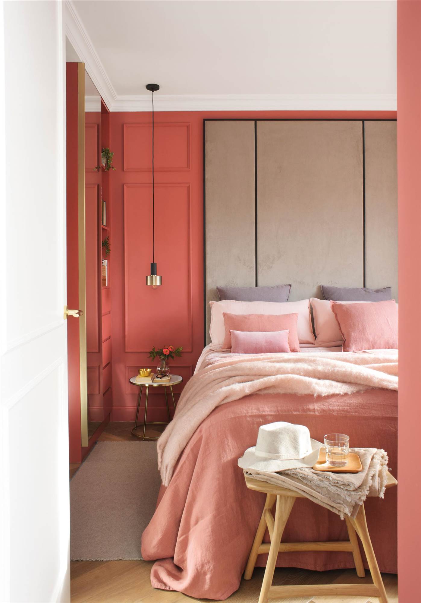 Dormitorio con paredes en color coral y cabecero hasta el techo tapizado. 