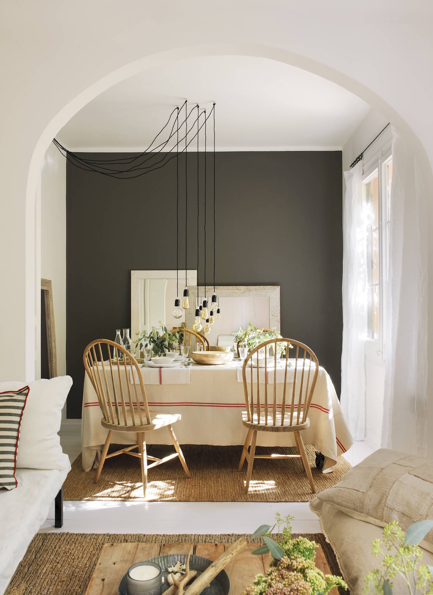 Comedor en blanco con sillas de madera, pared oscura y puerta con arco. 
