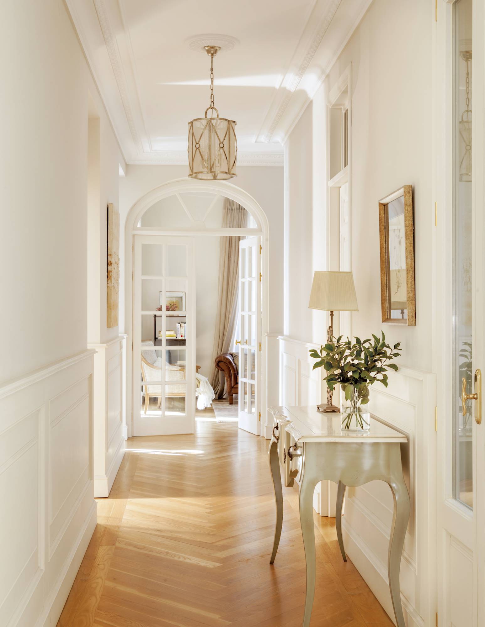 Pasillo blanco de estilo clásico con consola y suelo de madera. 