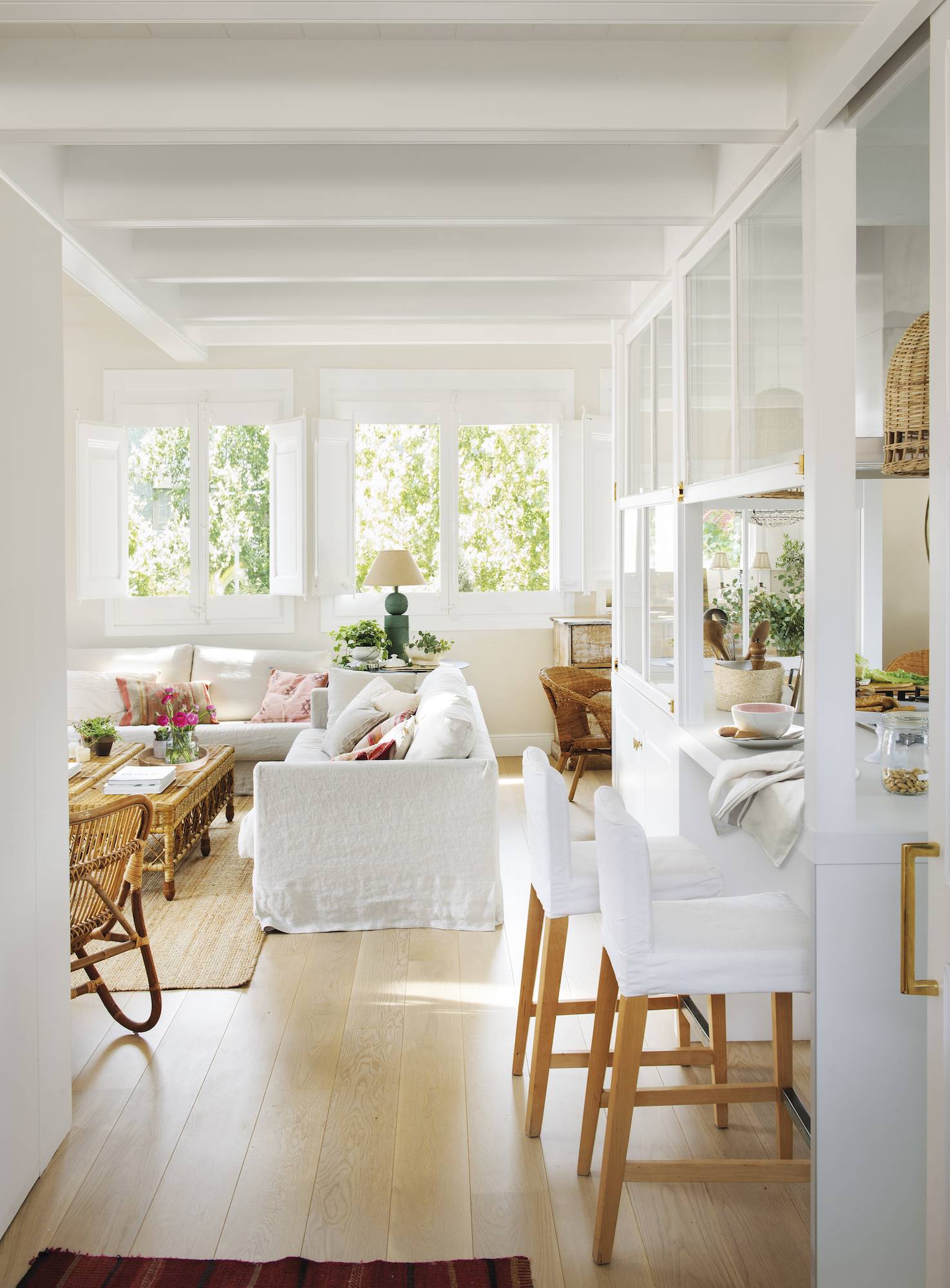 Un salón con barra hacia la cocina, taburetes y sofá en color blanco. 