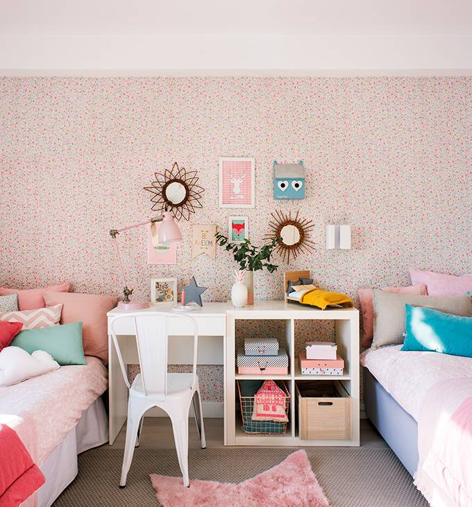 Dormitorio infantil con pared rosa con papel pintado de lunares, dos camas y un escritorio en medio. 
