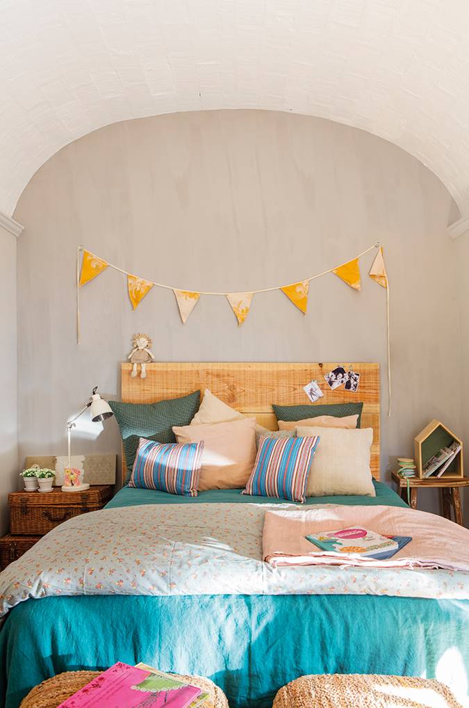 Dormitorio infantil con mesa amplia azul con cabecero de madera y guirnalda encima.