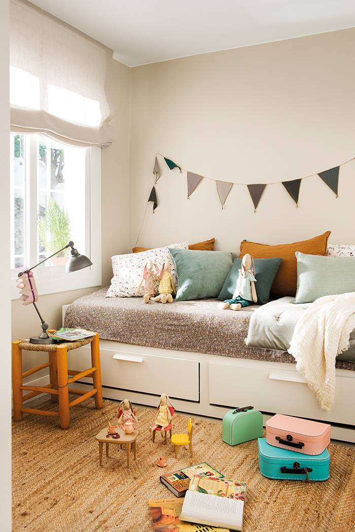 Dormitorio infantil con alfombra de fibra natural y cama decorada con el color rosa, lila, verde y marrón. 