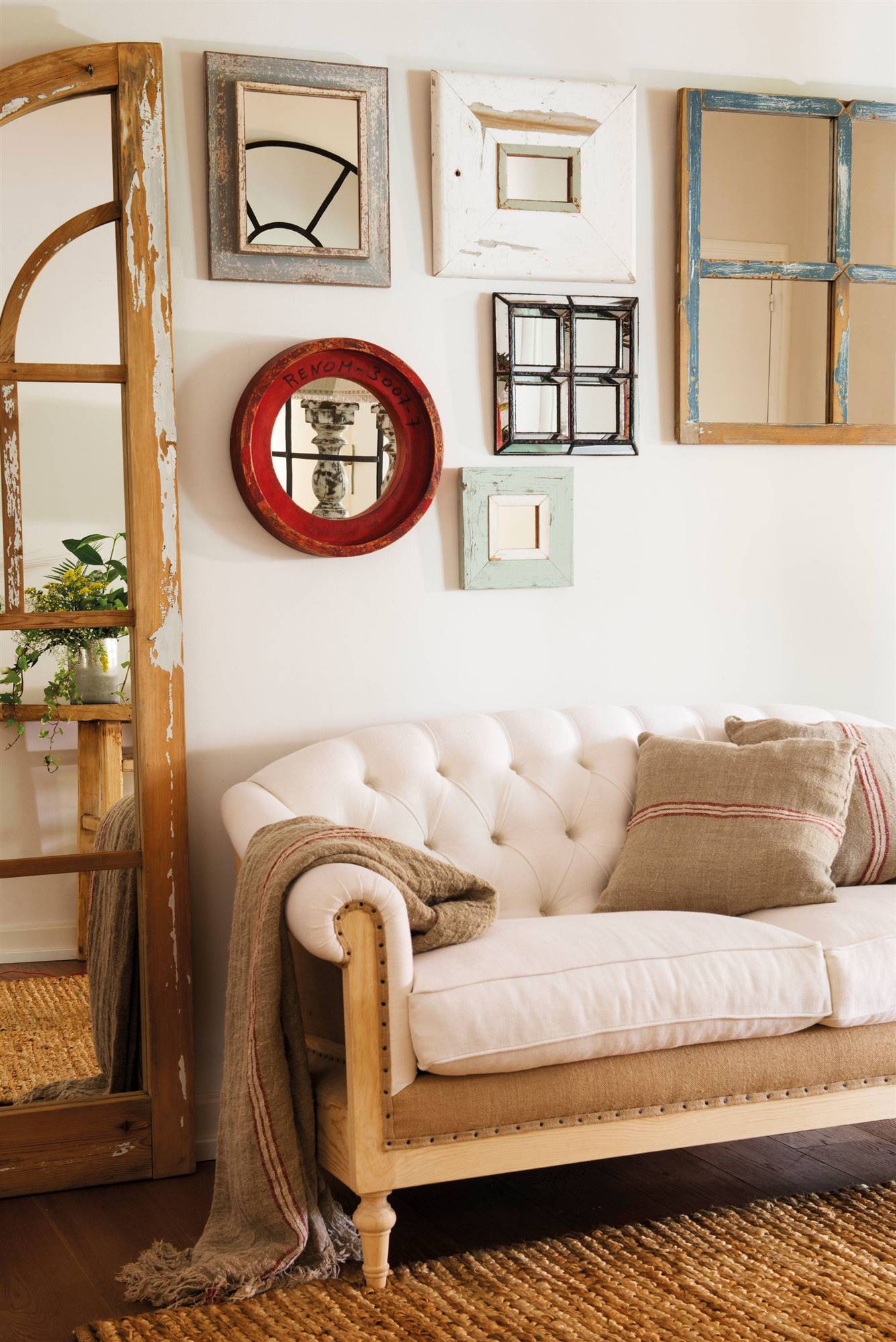 Zona de paso con pared decorada con espejos y sofá blanco chester