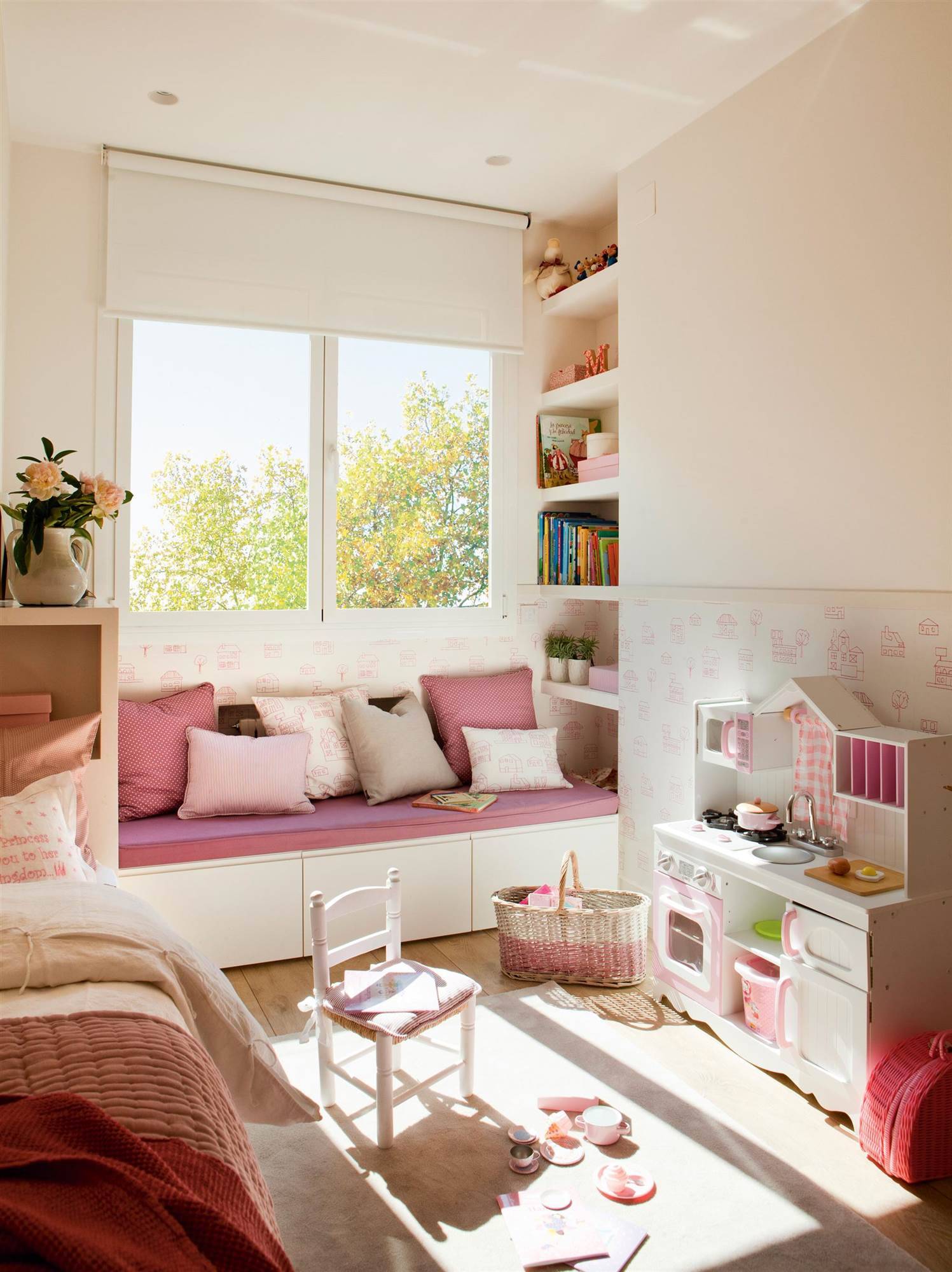 Habitación infantil en rosa con juguetes, arrimadero con papel pintado y banco bajo la ventana.