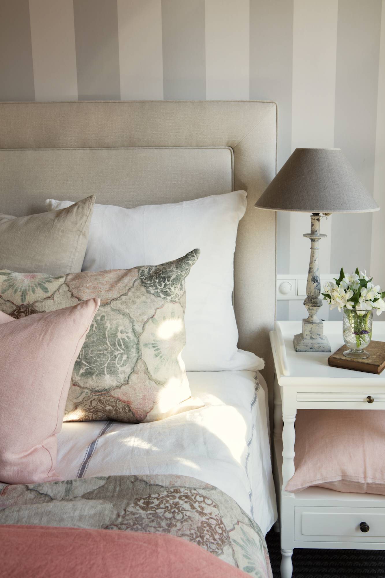 Dormitorio con cabecero tapizado y pared con papel pintado de rayas. 