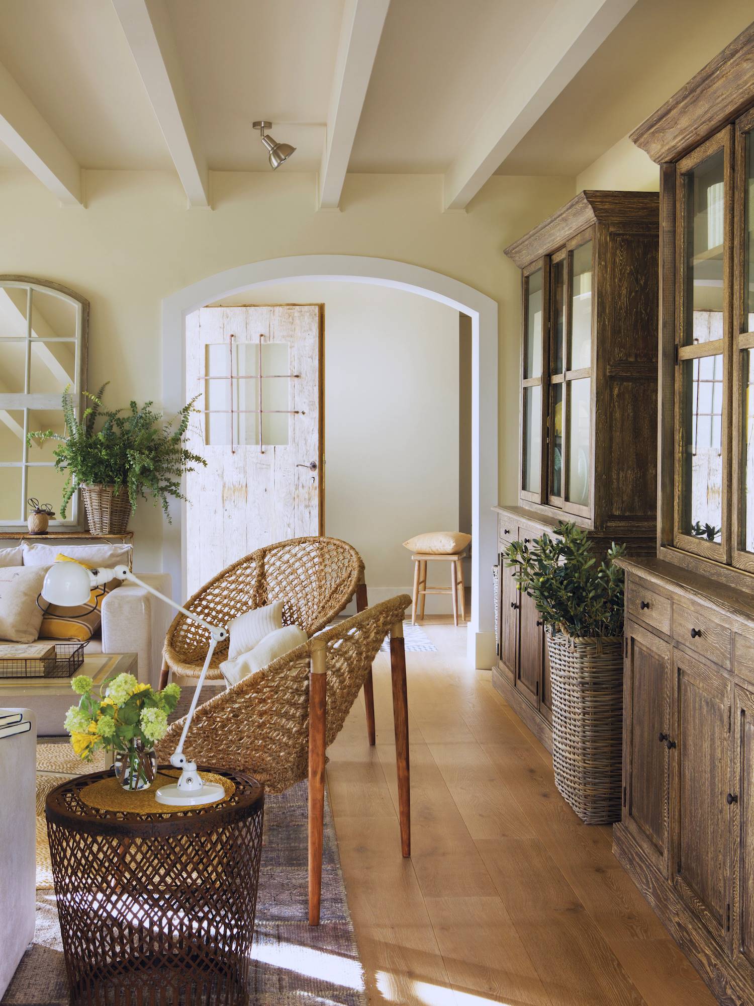 Salón con paredes beige y muebles de madera y butacas de fibras naturales. 