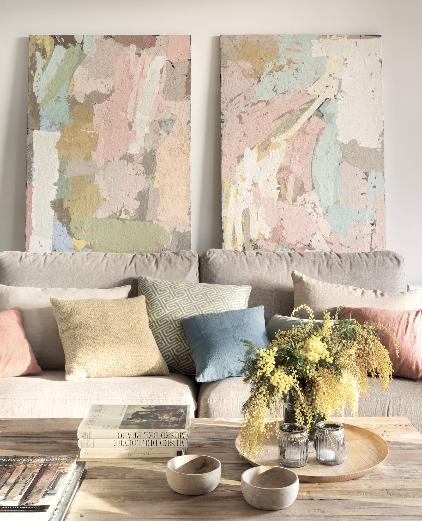 Salón con sofá beige y cojines de color pastel rosas, amarillos, azules y verdes. 