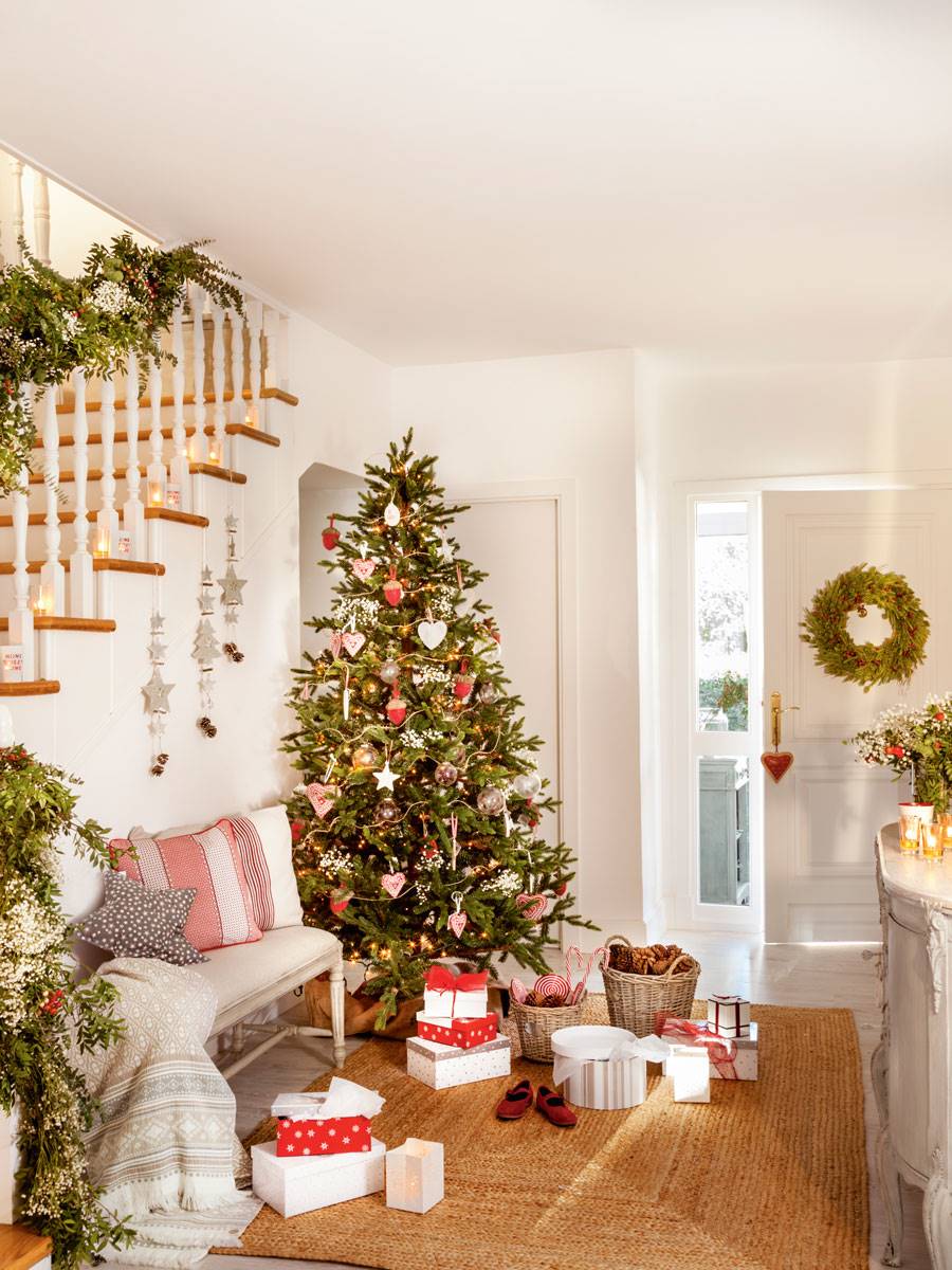 Recibidor blanco con alfombra de yute, banco y árbol de Navidad con adornos rojos.