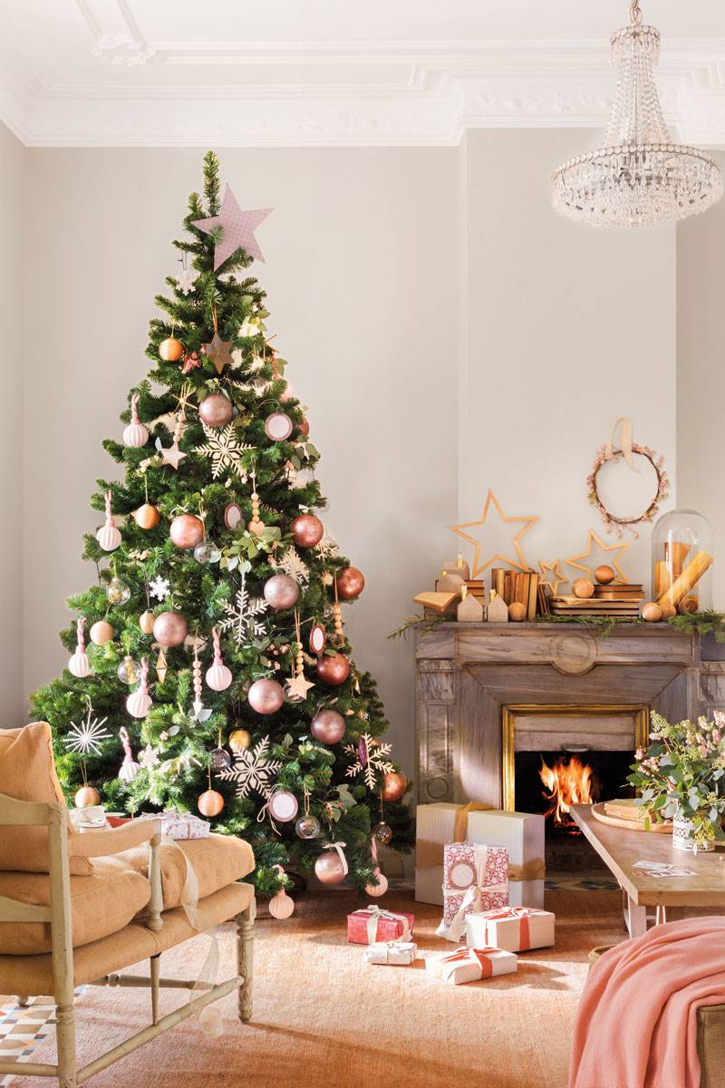 Salón clásico con chimenea y árbol de Navidad decorado con adornos rosados. 