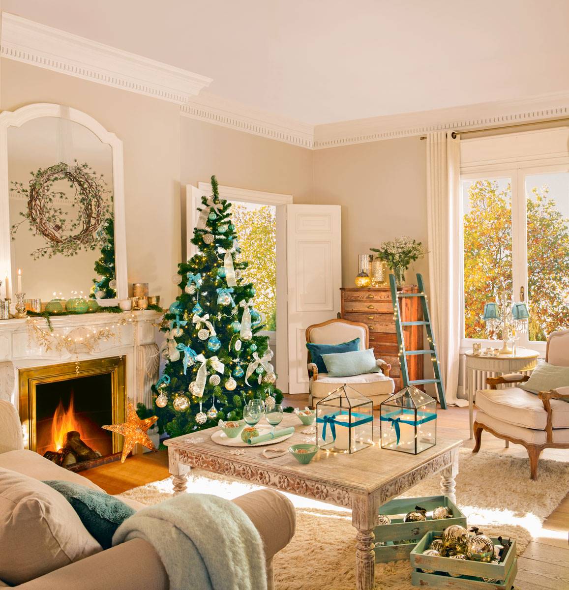 Salón clásico con chimenea, molduras, mesa de centro blanca, alfombra y árbol de Navidad decorado en azul.